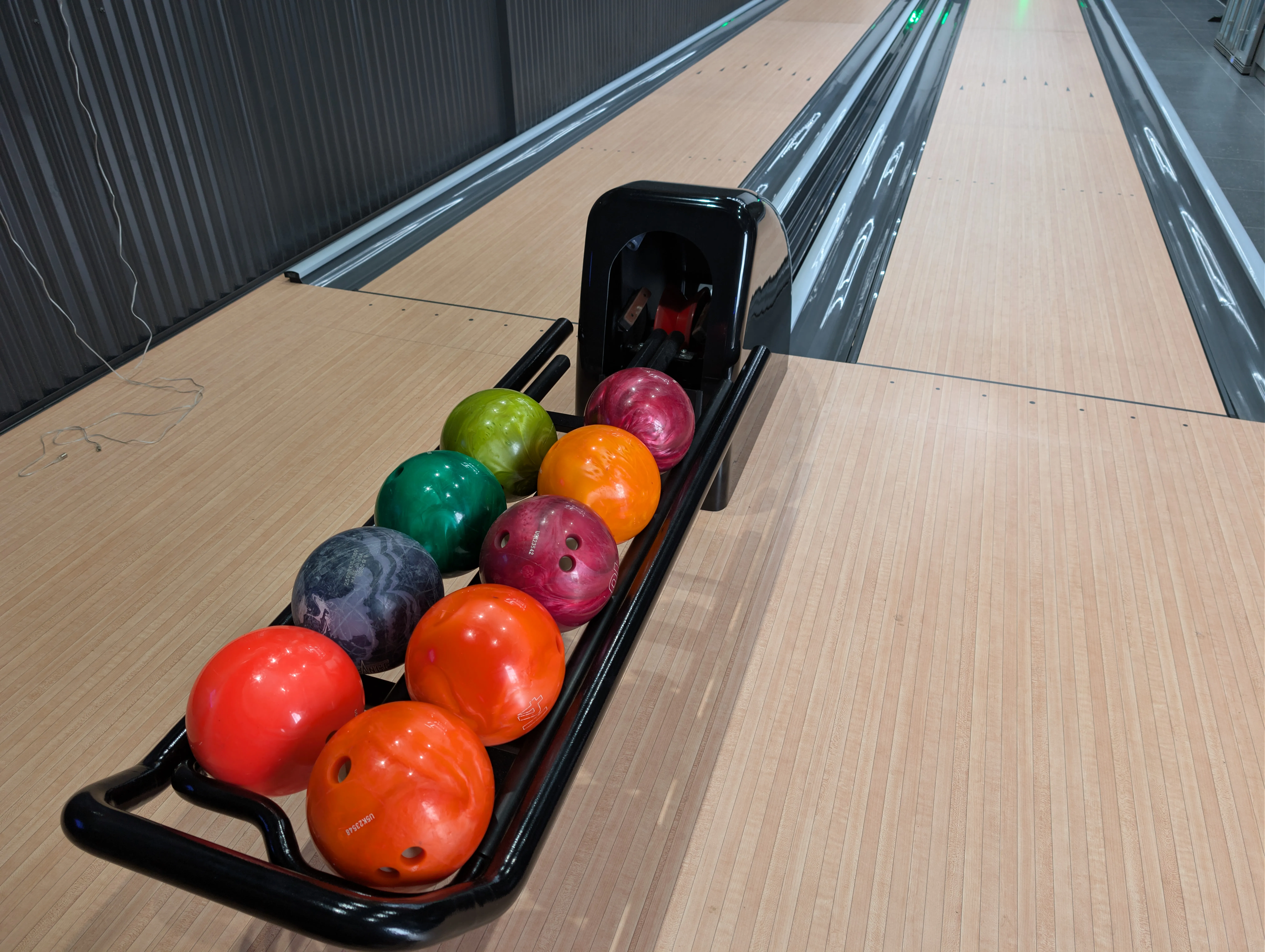 Colourful bowling balls on a black ball return between two private lanes