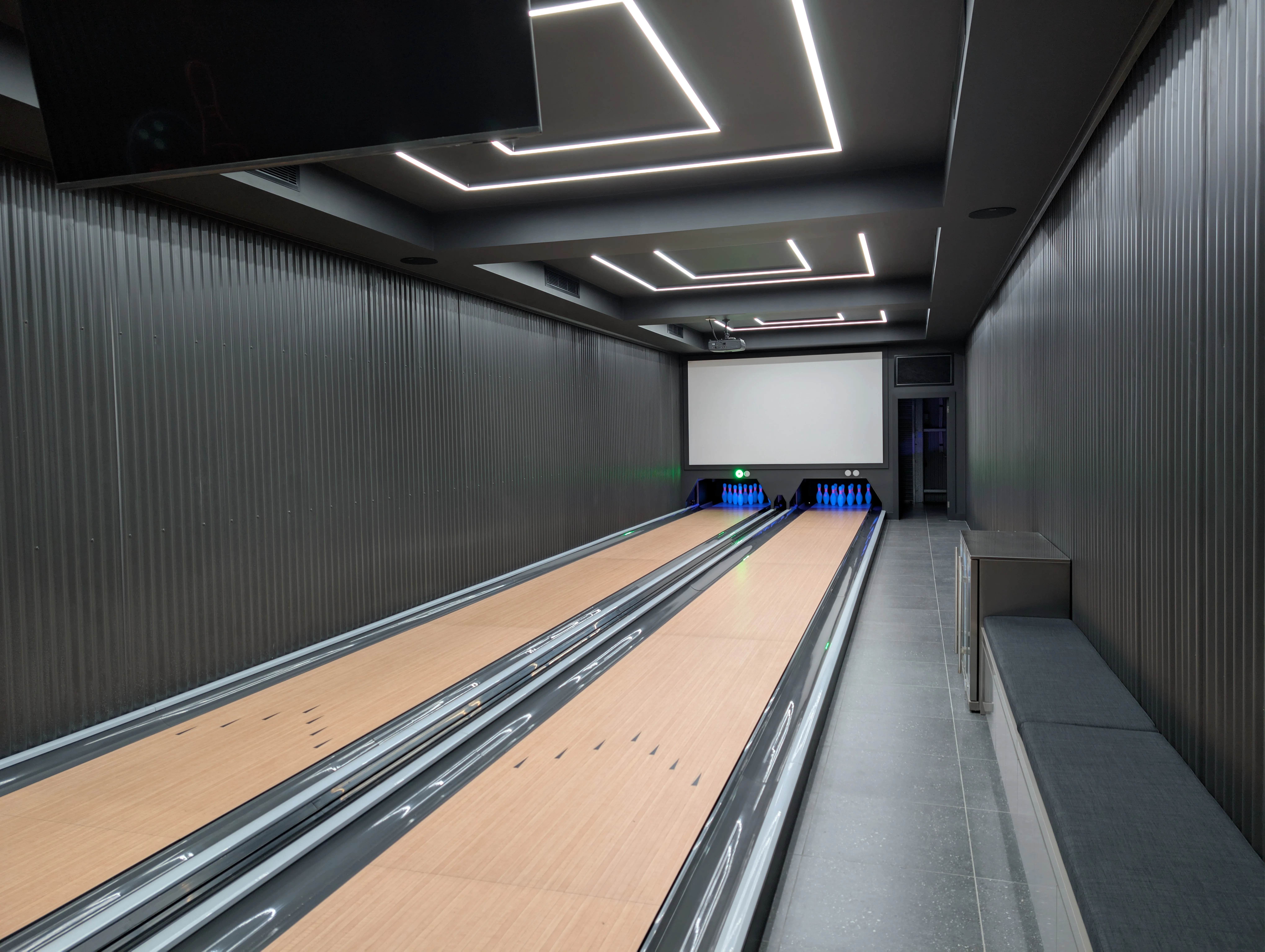 Wide view of two finished private bowling lanes running the length of a dark entertainment shed