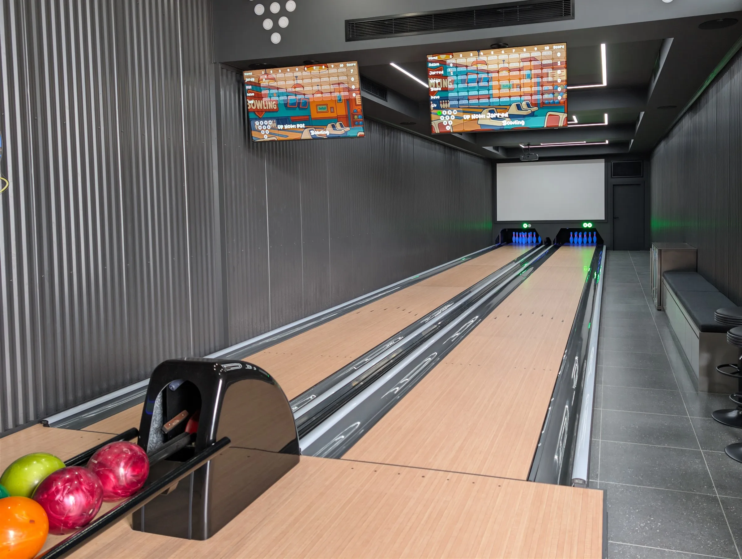 Private bowling room with live scoring screens, ball rack and seating alongside the lanes